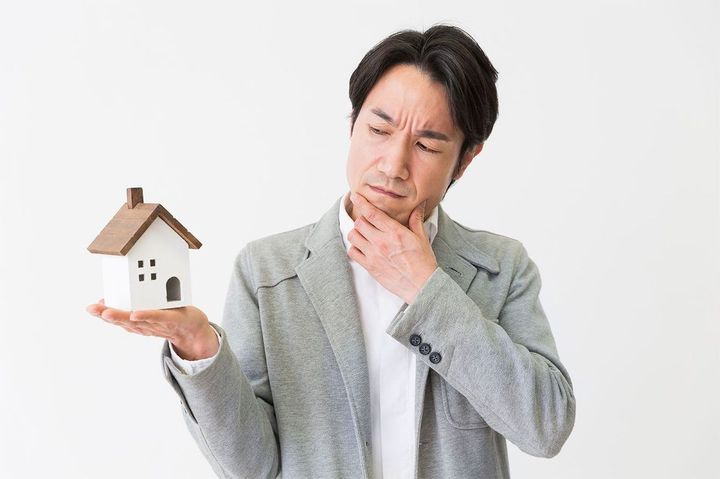 ミニチュアの家を持って悩む男性