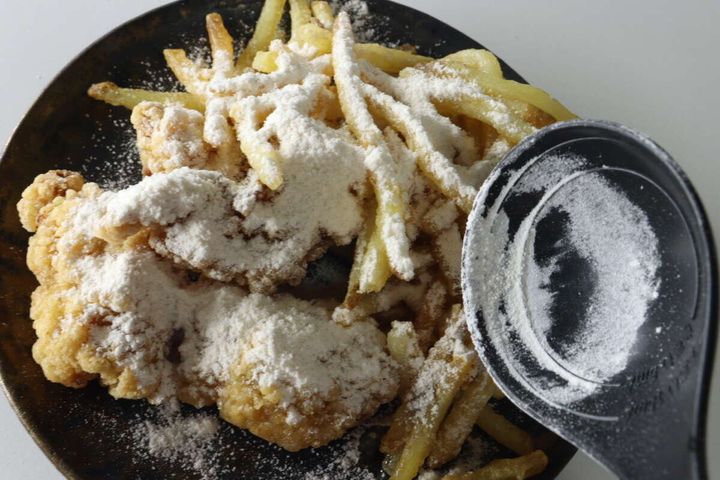 黒い皿に盛られた竜田揚げとフライドポテトに白いパウダーがたっぷりかかっている俯瞰