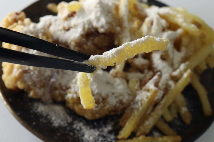 黒い箸でつまんだ、白いパウダーがかかったフライドポテトのアップ