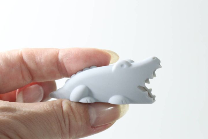 指でつまんで持ったグレーのワニ型歯ブラシキャップ
