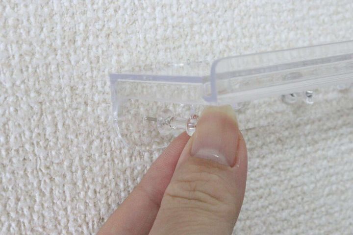 クリアスタンドをプッシュピンで壁に取り付けている手元