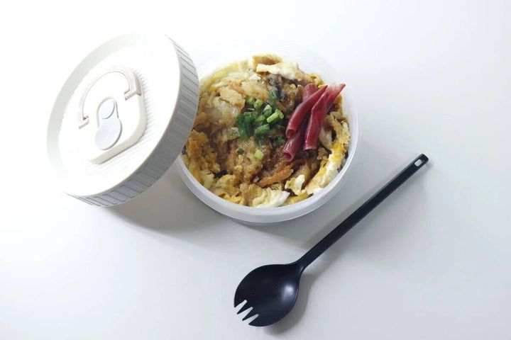 丼ものが盛られた丸い弁当箱とフタ、黒いスプーン