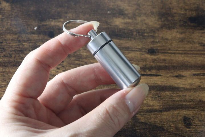 女性の指が、銀色のカプセルケースキーホルダーを掴んでサイズ感を示している