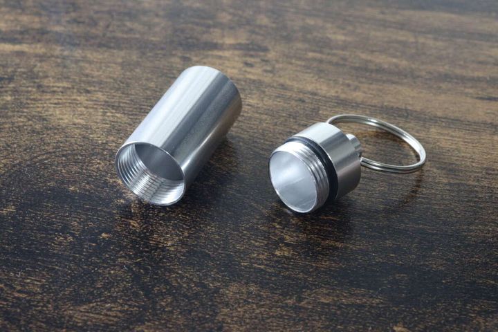 銀色のカプセルケースキーホルダーが、本体とキャップに分解されて置かれている