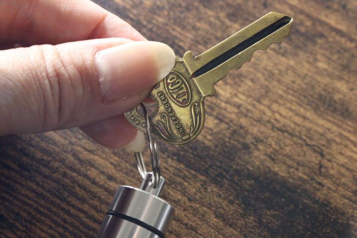 女性の指が、銀色のカプセルケースキーホルダーのリングにアンティーク調の鍵を取り付けている