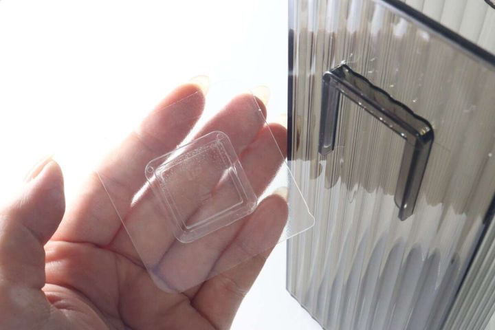 女性の手のひらに乗せられた透明な粘着シートと傘立て本体の一部