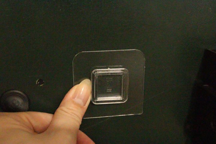 濃い緑色の壁に透明な粘着シートを指でしっかりと押し付けている様子