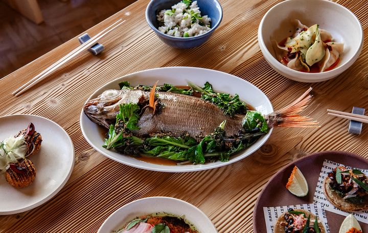 木のテーブルに並ぶ、ハーブを添えた魚の丸焼きや小鉢、タコスなど「ナキムシ」2階の料理