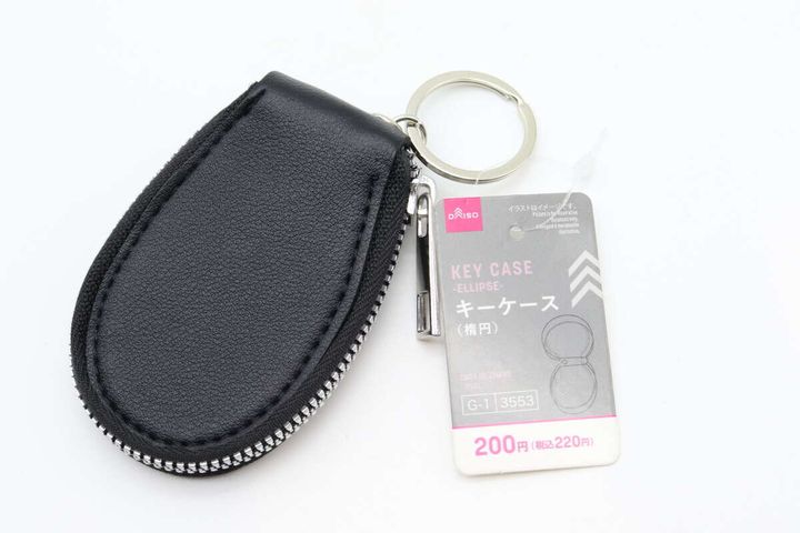 黒い楕円形のキーケースと商品タグが白い背景に置かれている