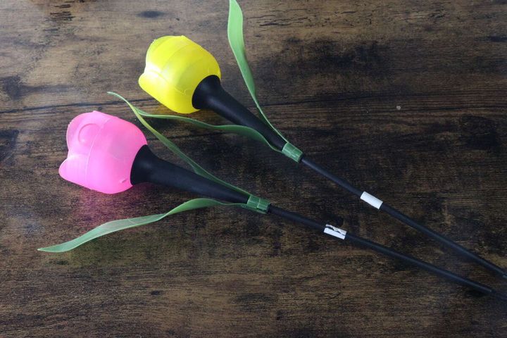 ピンクと黄色の花型ソーラーライト2本が木目のテーブルに並べられている