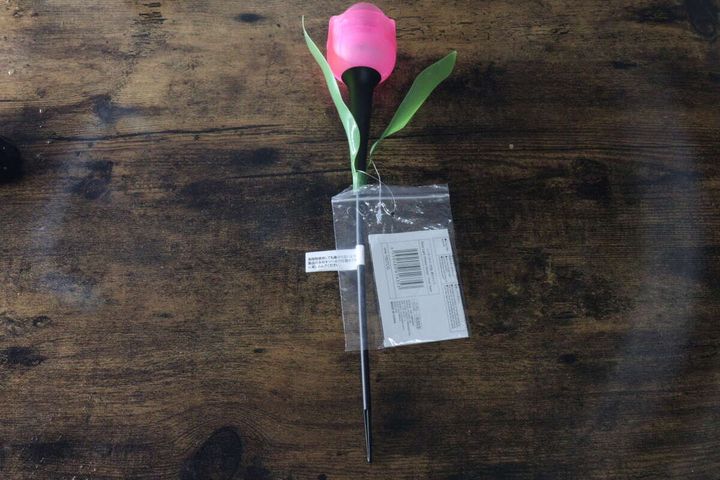 ピンクの花型ソーラーライトが透明な袋に入った状態で木目のテーブルに置かれている