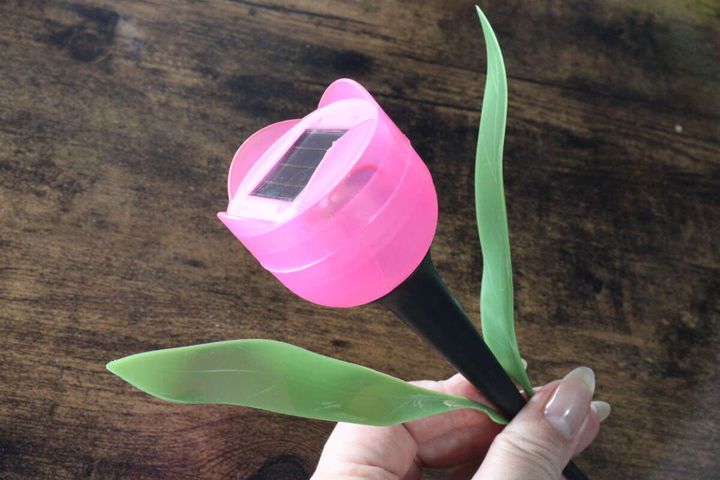 女性の手がピンクの花型ソーラーライトを持ち、ソーラーパネル部分が上を向いている