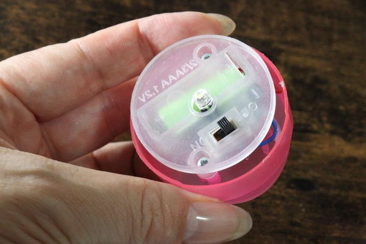女性の手がソーラーライトの底部分を開け、電源スイッチと電池が見えている状態