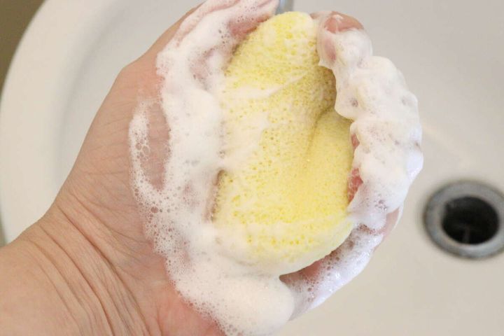 手のひらで黄色い洗顔パフを握り、洗顔料を泡立てている様子