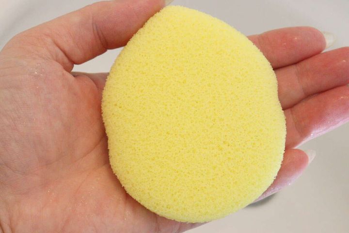 水を含んで膨らんだしずく形の黄色い洗顔パフを手のひらに乗せている