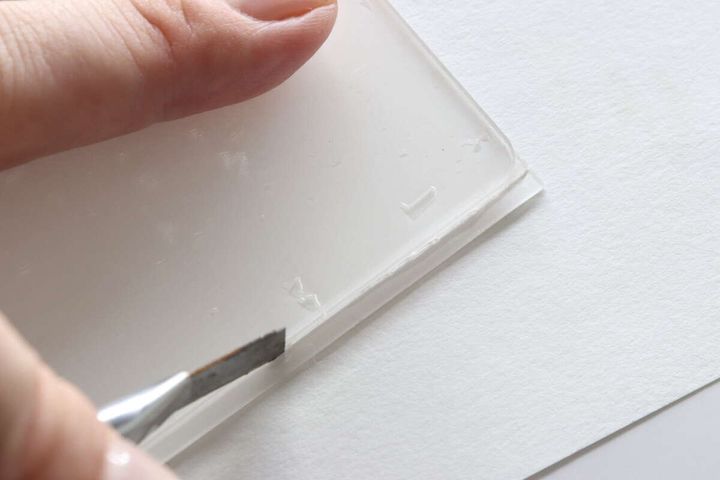 アクリル板に貼った粘着シートの余分な部分をカッターで切り取っている様子