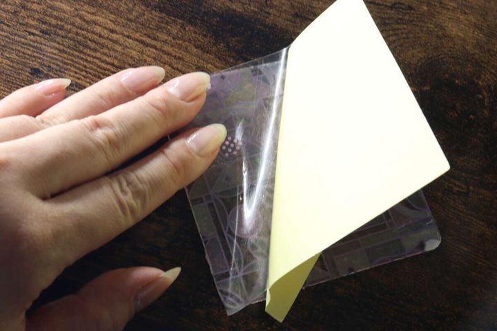 アクリル板に貼ったデザインシートの上から保護フィルムの剥離紙を剥がしている指先