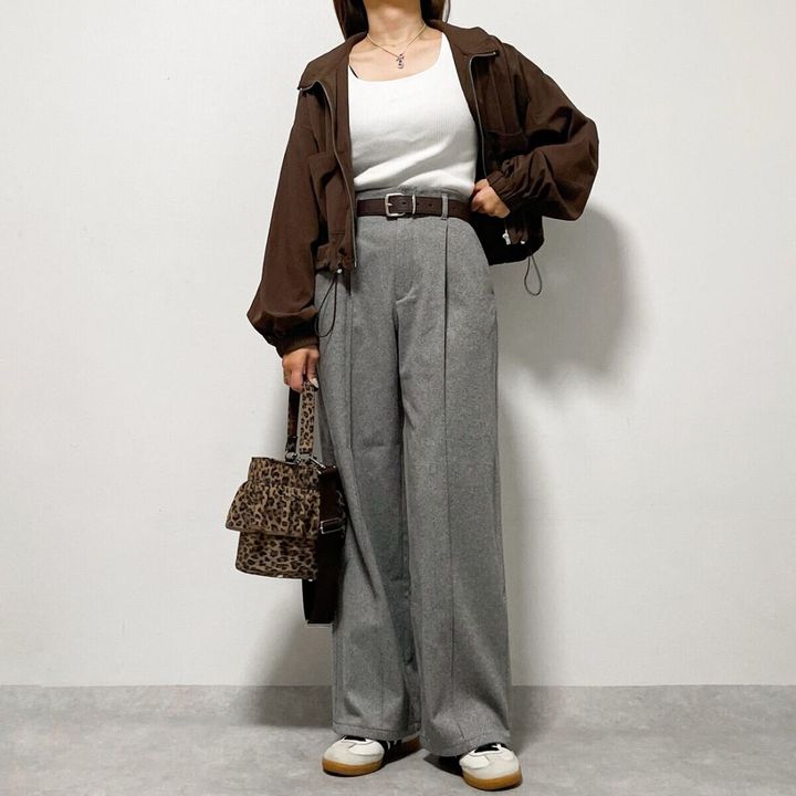 焦茶色のブルゾンとグレーのワイドパンツを着用し、レオパード柄のミニバッグを持つ女性