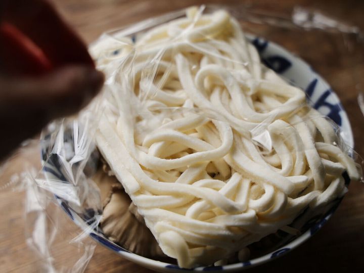 青い模様の器に入ったきのこの上に、袋に入ったままの冷凍うどんが乗せられている
