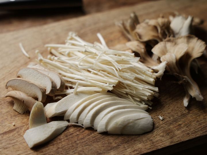 まな板の上に、えのき、しめじ、エリンギなど数種類のきのこが食べやすい大きさに切られて並べられている