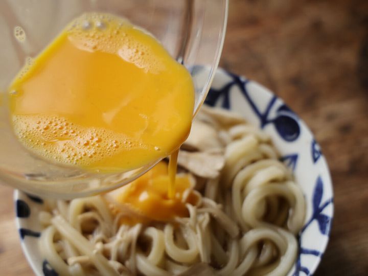 電子レンジで加熱後のうどんとキノコが入った器に、泡立てた溶き卵が上から回し入れられている