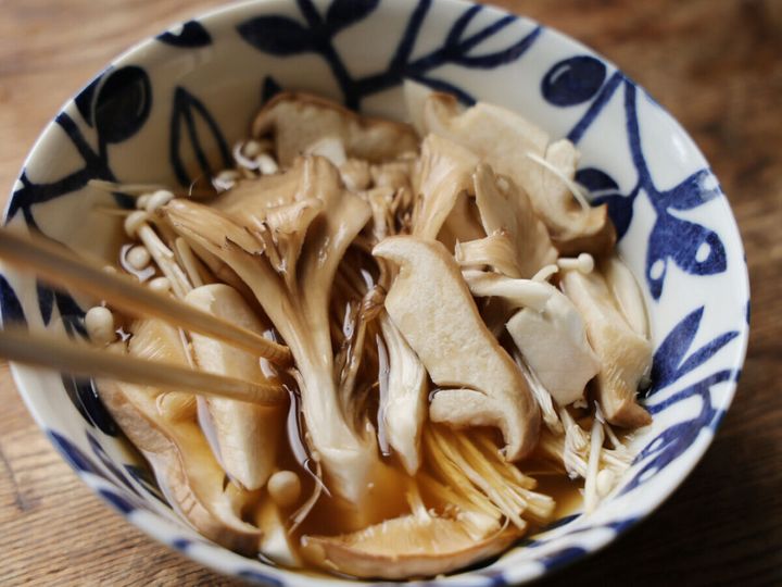 青い模様の器に、めんつゆと水、片栗粉を混ぜたものの中に、切ったきのこが入れられ、箸で混ぜている