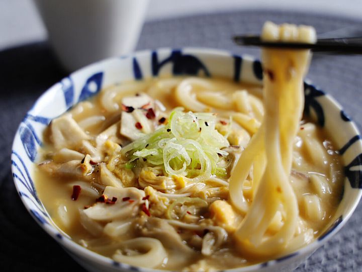 完成したきのこのかき玉うどんを箸で持ち上げている様子。刻みネギと唐辛子がトッピングされている