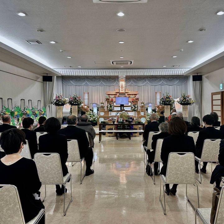 葬儀会場で、祭壇に向かって椅子に座る参列者たちの後ろ姿。