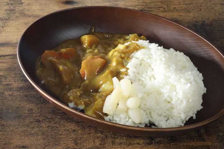 木目調の皿に盛られたカレーライスと、ご飯の横に添えられた花らっきょう