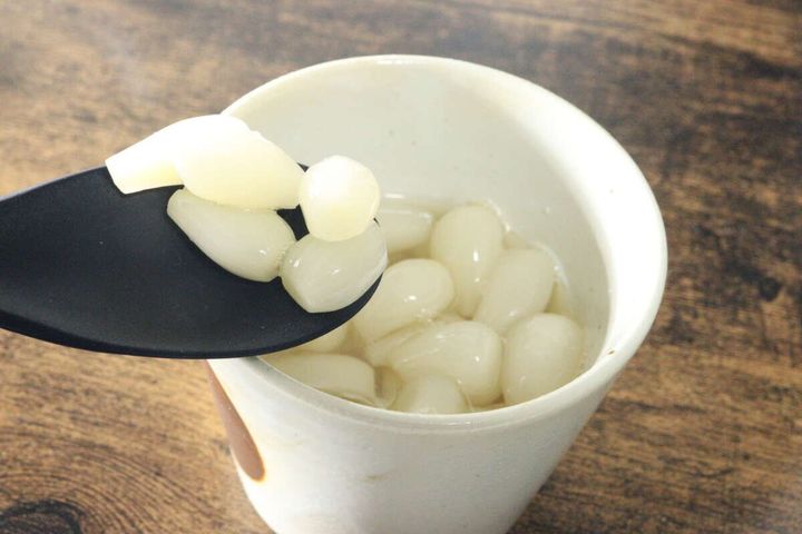 白い湯呑みに入った花らっきょうを黒いスプーンで数粒すくい上げている