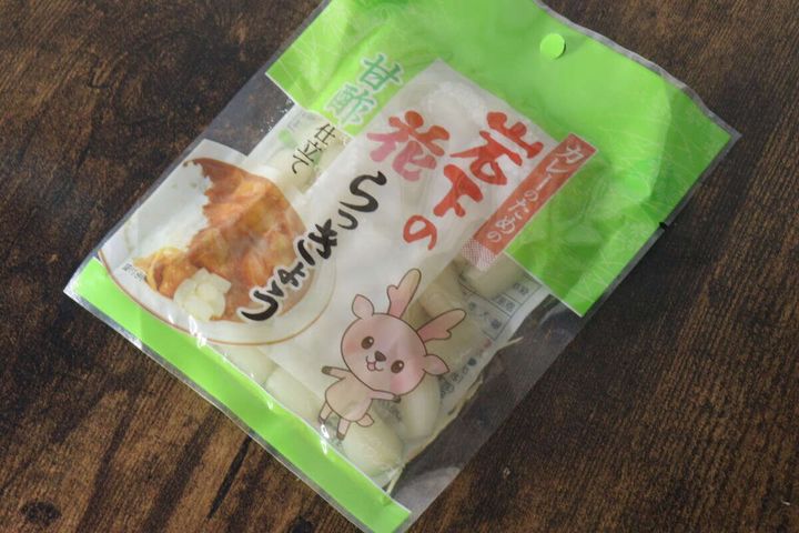 緑色のパッケージに入った岩下のカレーのための花らっきょうが木目のテーブルに置かれている