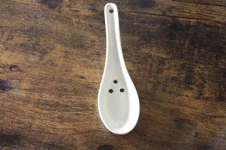 白い陶器製の穴あきレンゲが木目のテーブルに置かれている俯瞰