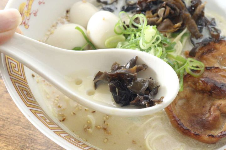 白い陶器製の穴あきレンゲでラーメンの具材（キクラゲ）をすくっているクローズアップ