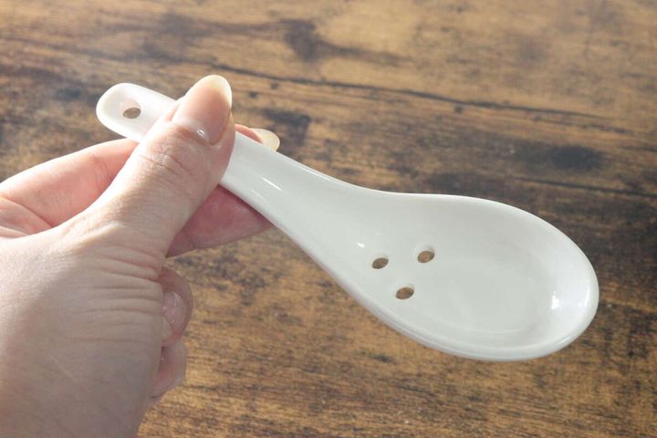 女性の指が白い陶器製の穴あきレンゲを横から持っている