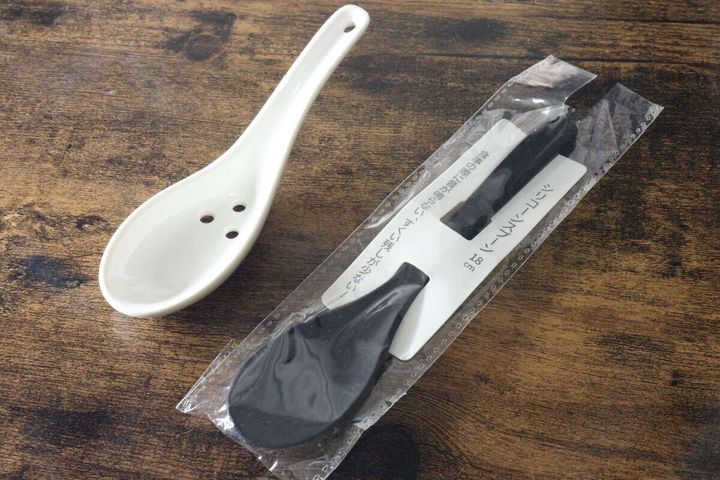 白い陶器製の穴あきレンゲとパッケージに入った黒いシリコーンスプーンが並べられている