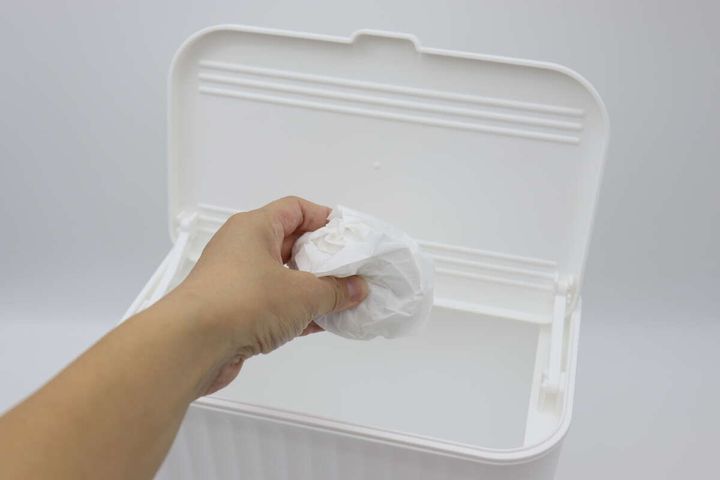 フタが開いた白いゴミ箱に、右手が丸めた白い紙を捨て入れている