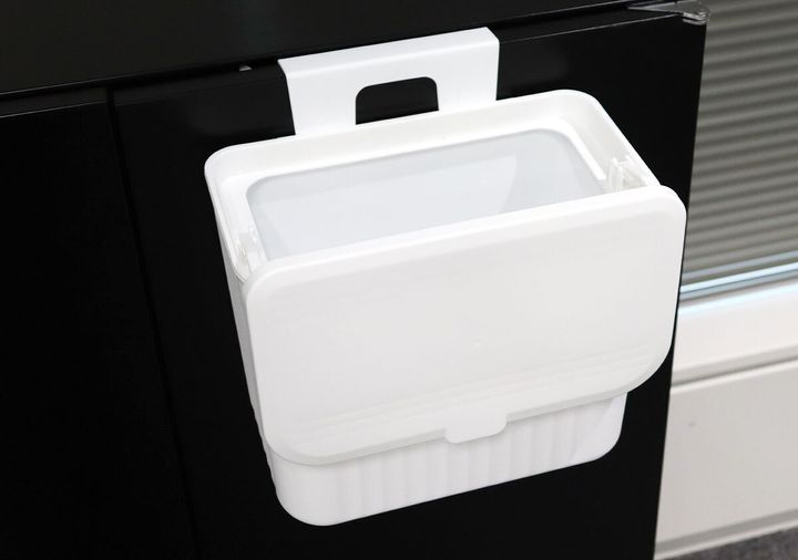 黒い扉に掛けられた白いゴミ箱のフタが、手前側に開いている