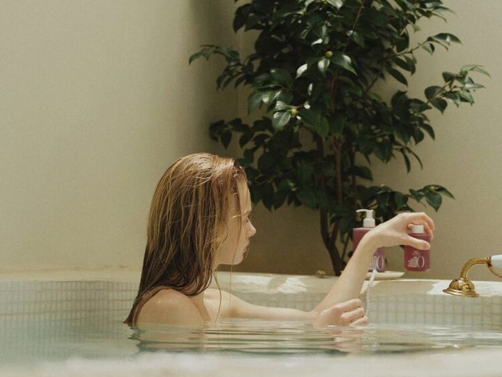 浴槽の中でANILLOのボトルを手にする、濡れた髪の女性