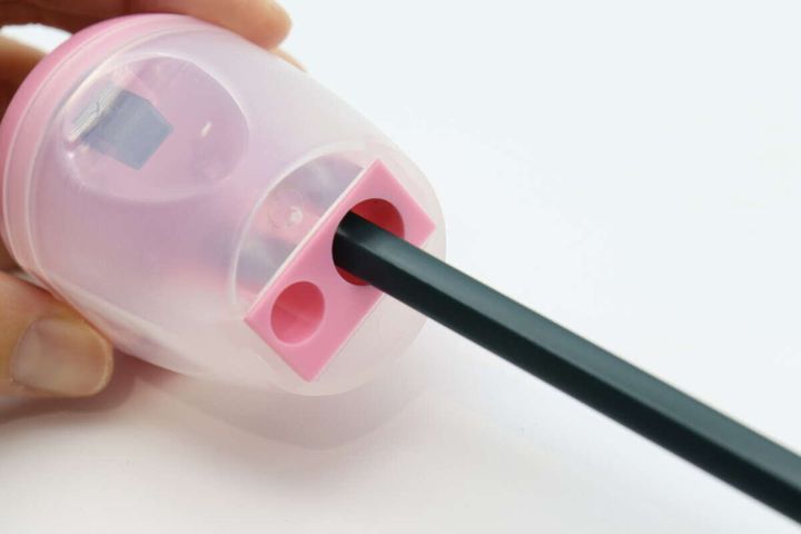 黒い鉛筆をゴミ箱型鉛筆削りの穴に差し込んでいる手元