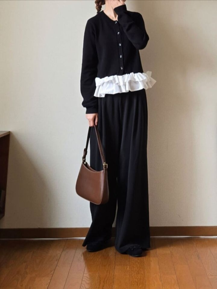 黒のフリルペプラムトップスとワイドパンツを着用し、ブラウンのショルダーバッグを持つ女性