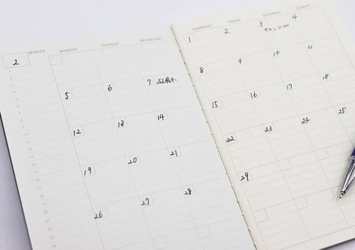 開かれたスケジュール帳のマンスリーページに予定が書かれている