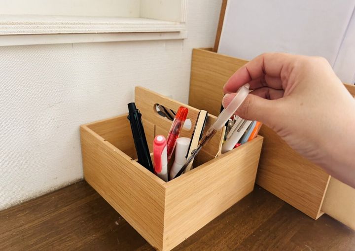 木のペン立てから白いペンを取り出そうとしている女性の手元