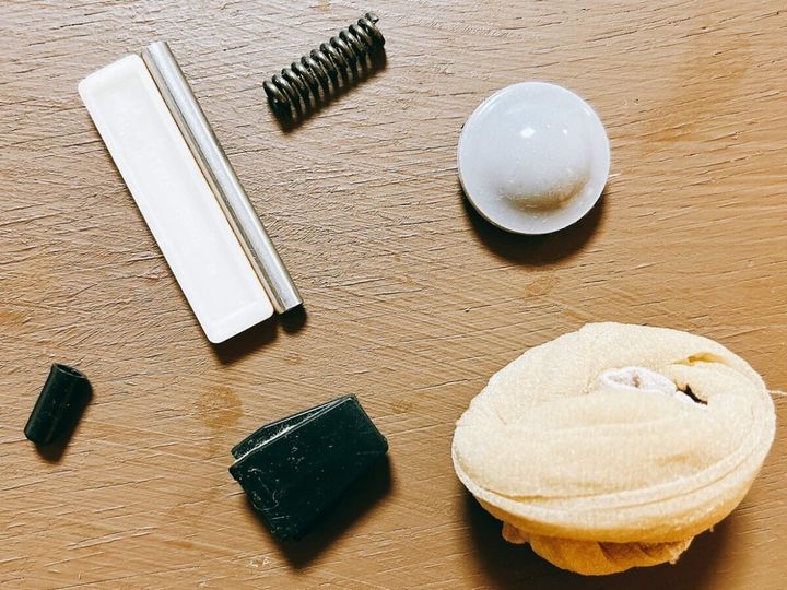 木目調のテーブルに置かれた用途不明の白い板や金属バネなどの部品