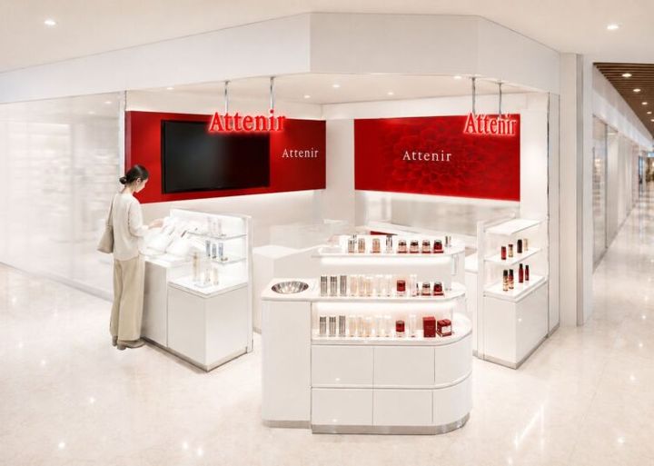 赤い壁面のモニターと化粧品が並ぶ、アテニアの売場のイメージ