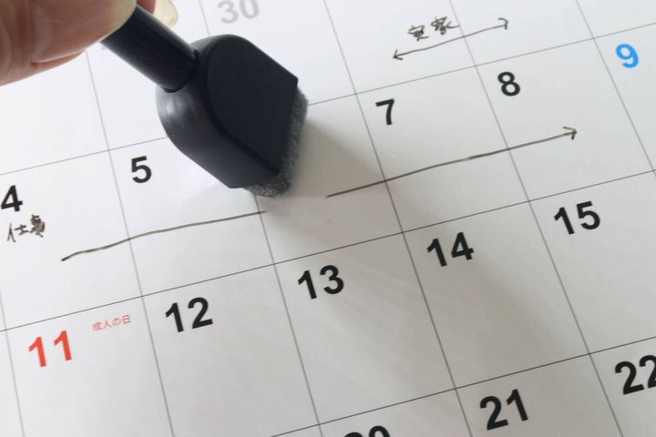 黒いイレーザーでダイソーのホワイトボードカレンダーに書かれた文字を消している。