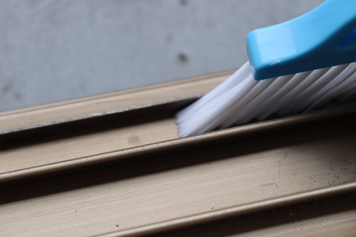 青いサッシブラシを縦にして、サッシの細い溝を掃除している様子