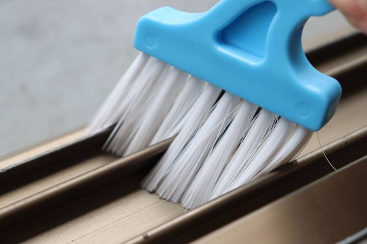 青いサッシブラシで汚れた窓のサッシのレールを掃除している様子