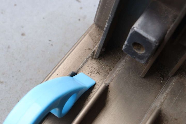 青いサッシブラシのスクレーパー部分で、サッシの頑固な汚れを削り落としている