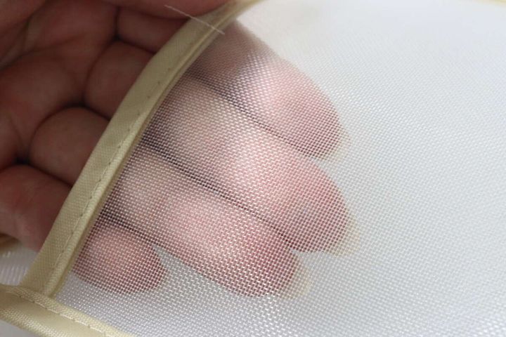 指でメッシュ素材を広げ、透け感と通気性を示している。