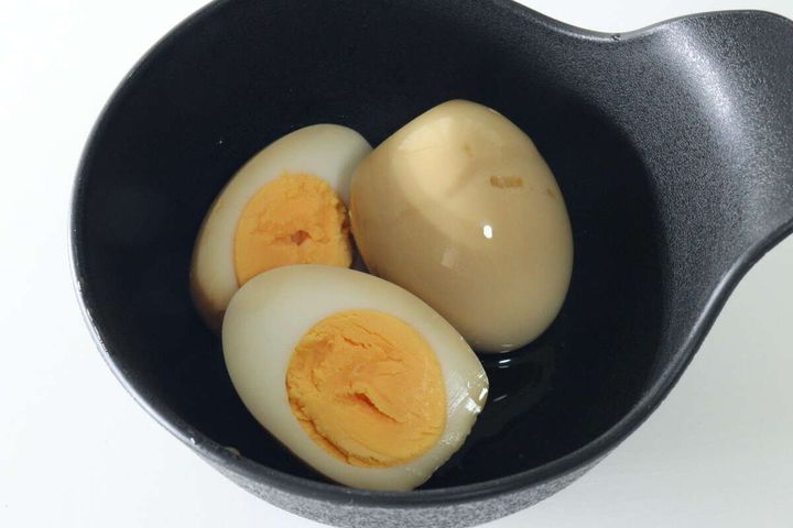 黒い器に盛られた、半分にカットされた煮卵と丸ごとの煮卵が3つ